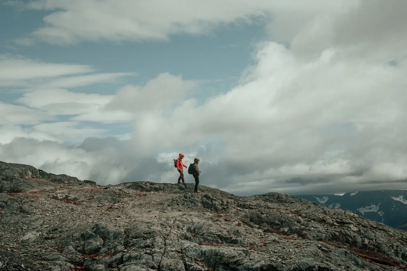 Two small figures crossing a rocky mountain landscape