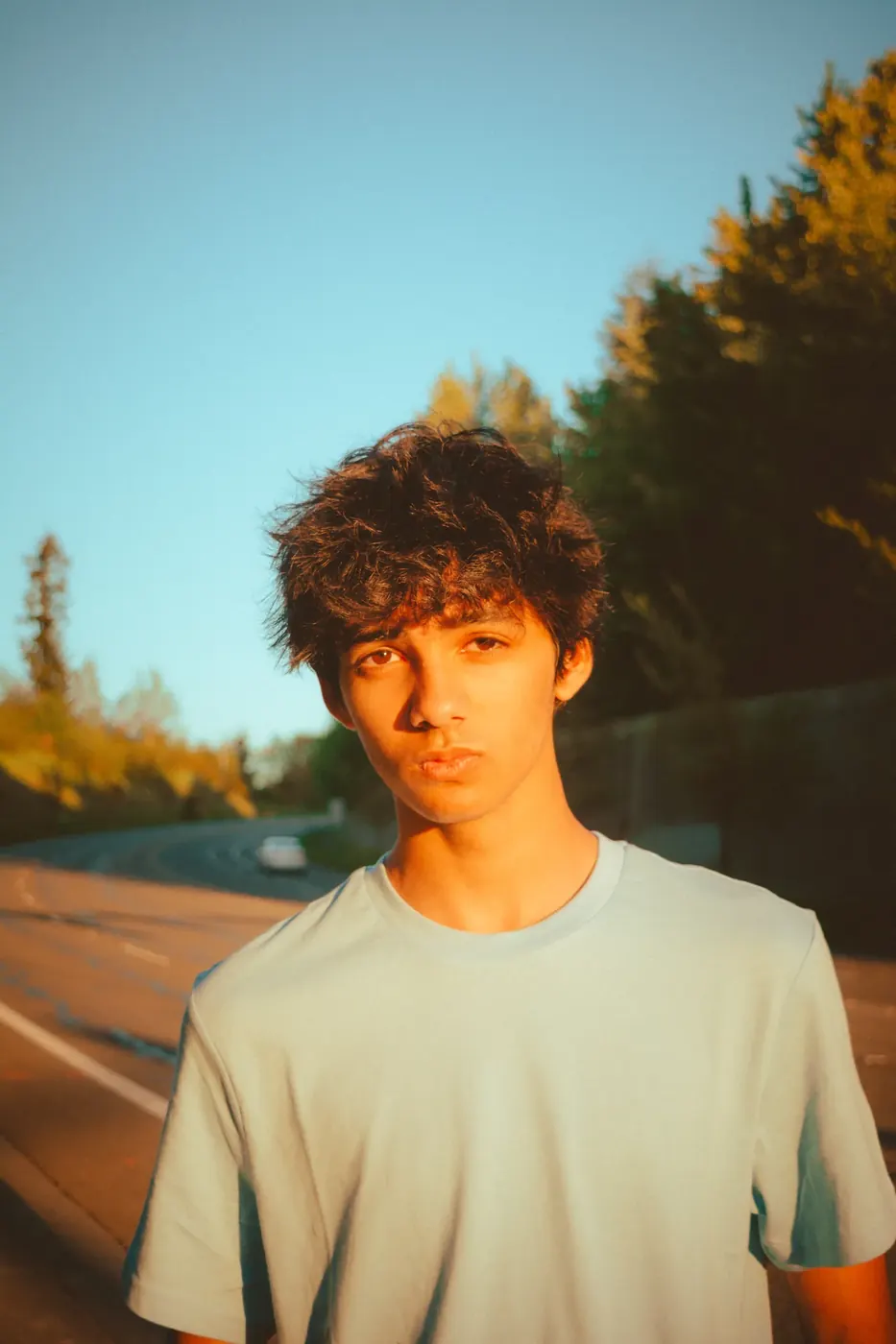 A young man illuminated by warm evening light beside a winding road