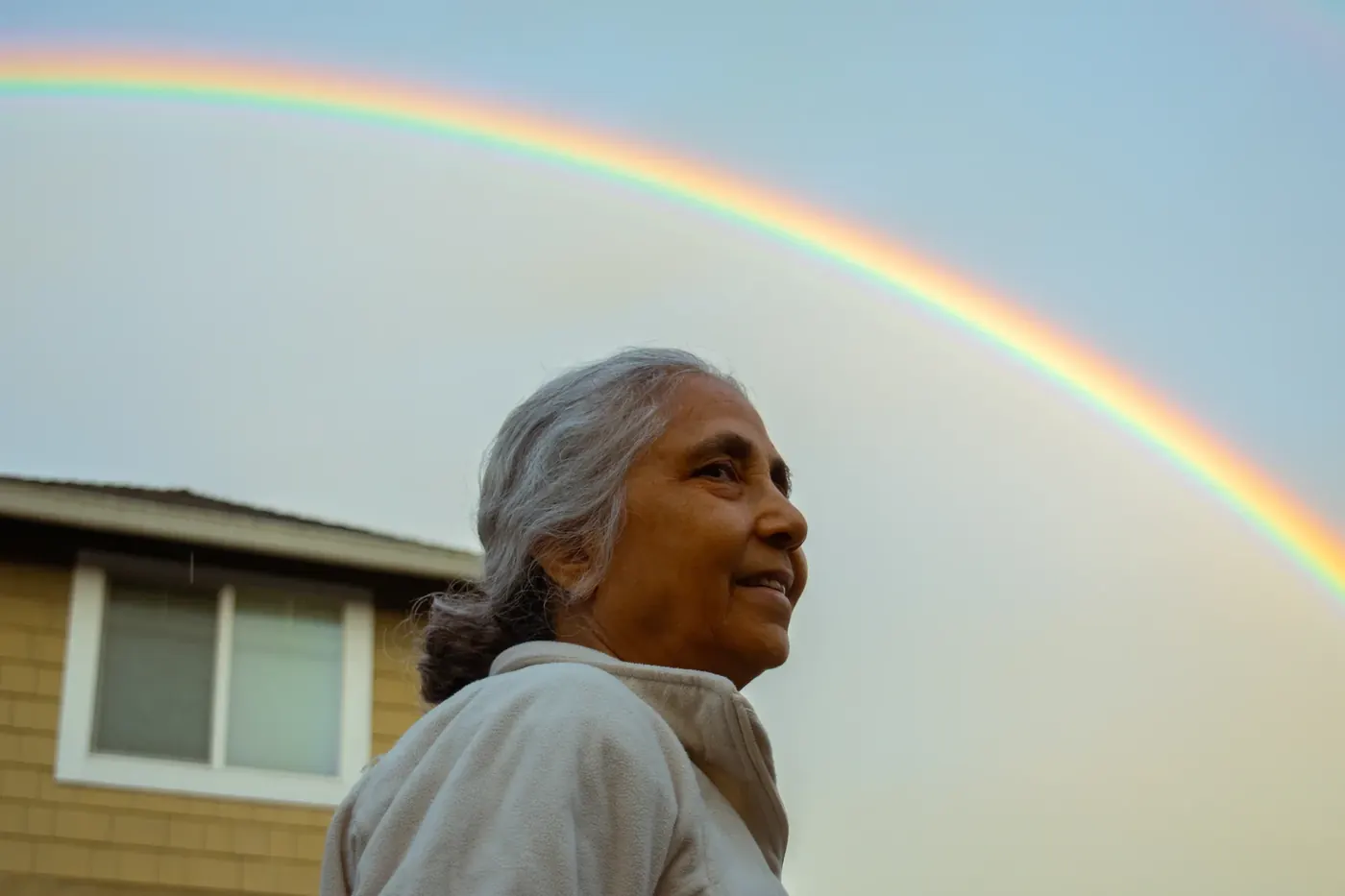 A close portrait of a smiling woman beneath a vivid rainbow