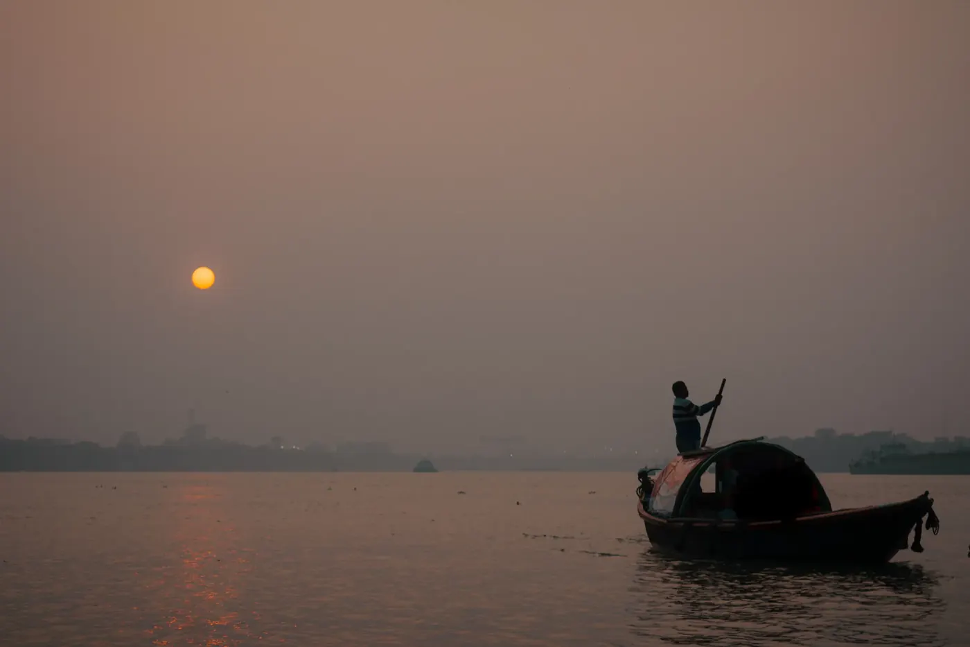 A small boat passing beneath the orange sun in a hazy sky