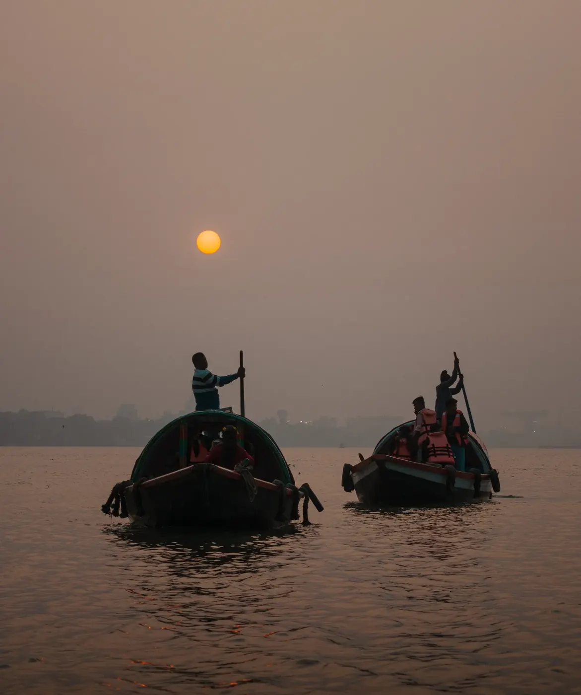 Two boats moving beneath the orange sun in a hazy sky