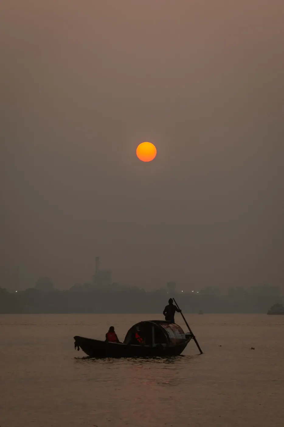 A boat crossing the water beneath the orange sun in a hazy sky