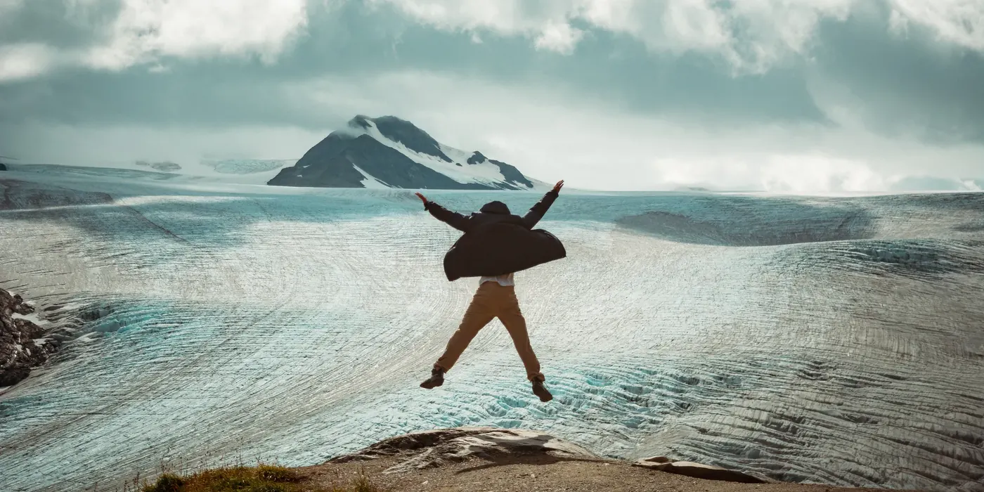 A person leaping above a dramatic glacier view