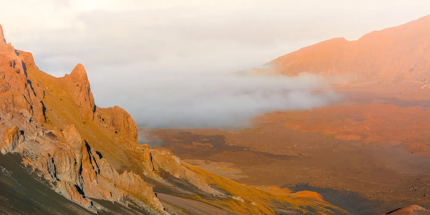 Orange mountain cliffs emerging from low clouds