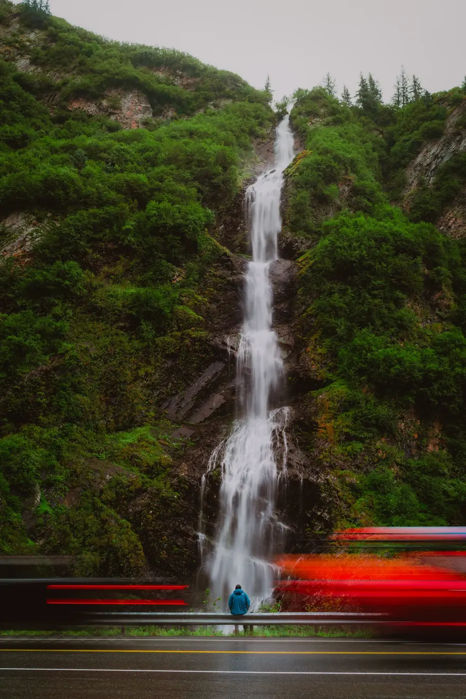 A long waterfall, a lone viewer, and passing red light trails
