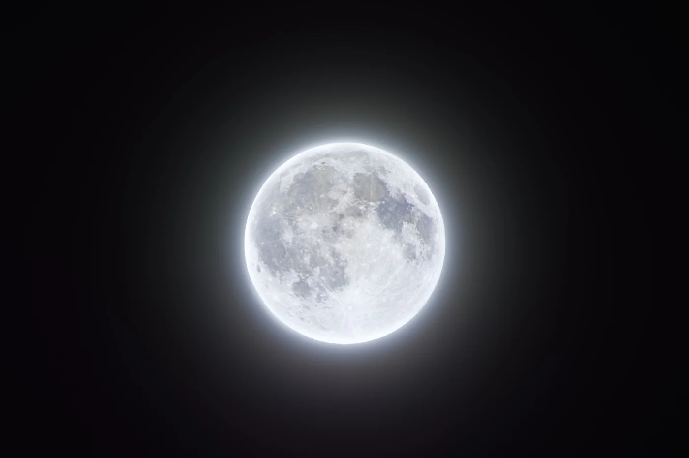 A full moon surrounded by a pale halo against a dark sky