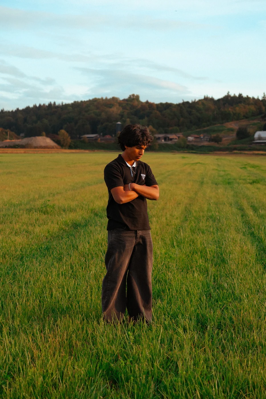 A person dressed in black standing with folded arms in a green field