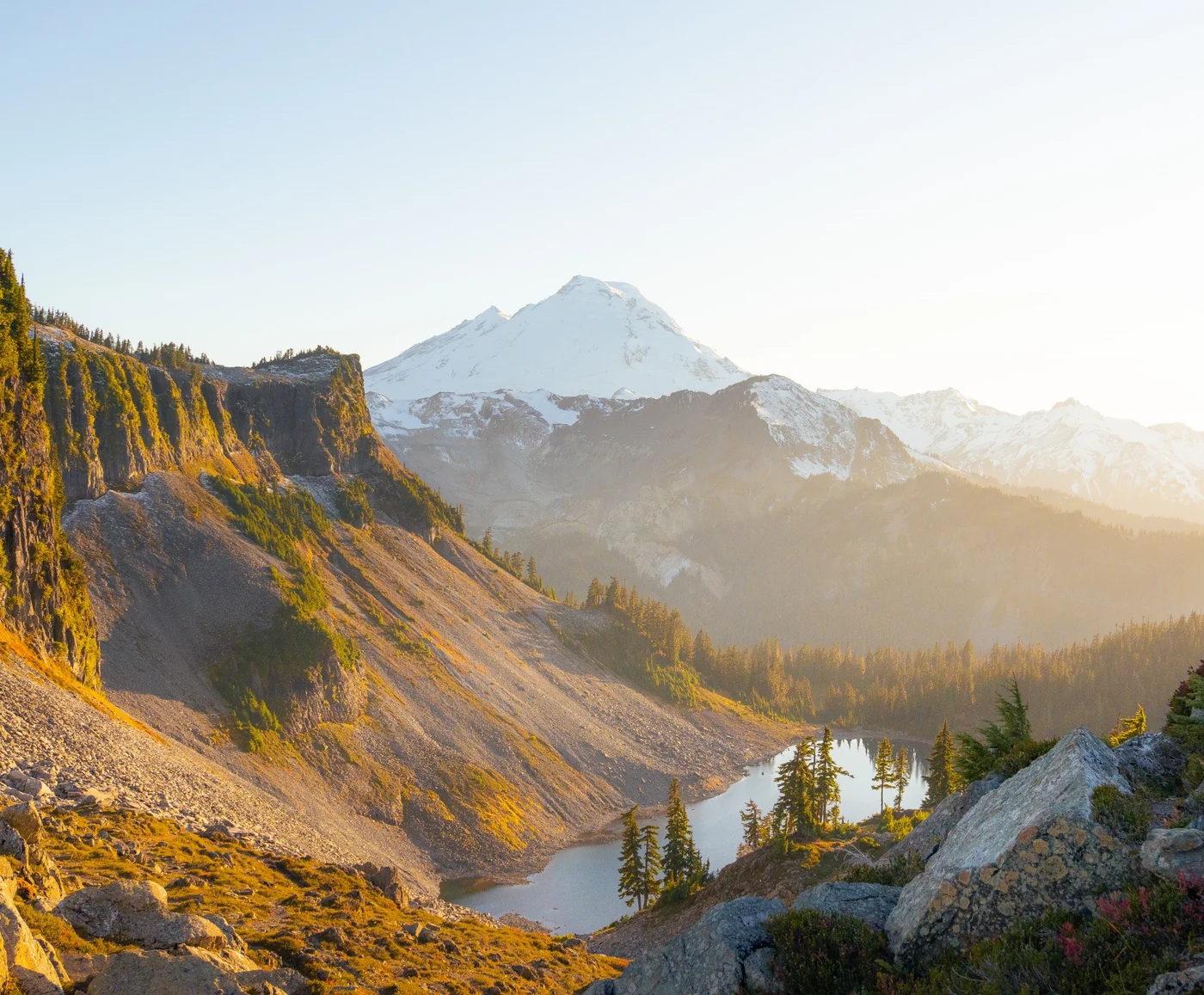 Warm light crossing a rocky mountain basin and a small lake beneath a snowy peak