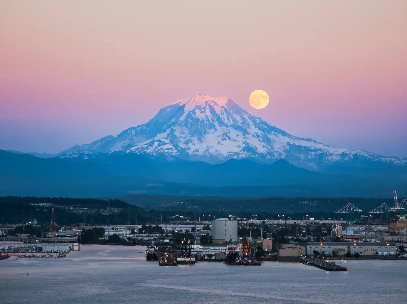 The moon rising beside a snow-capped mountain at dusk